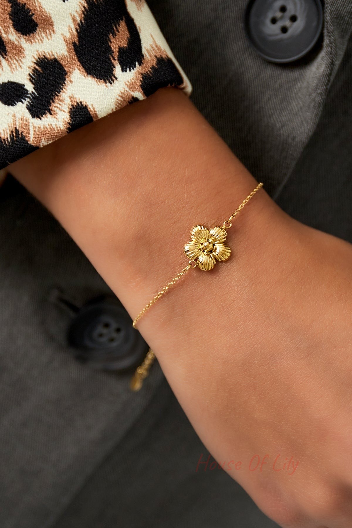 Close-up of gold daisy charm bracelet worn on wrist with leopard print sleeve and dark jacket showing elegant, youthful style