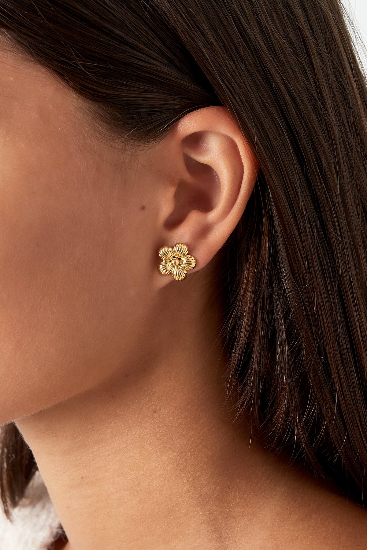Close-up of gold fluted flower stud earring worn on woman's ear with dark hair
