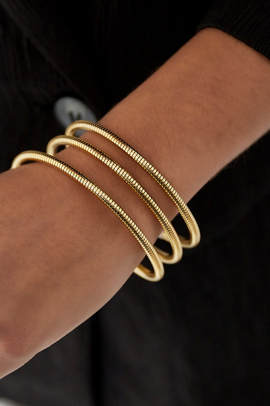 Close-up of a gold spiral coil cuff bracelet worn on wrist with black sleeve