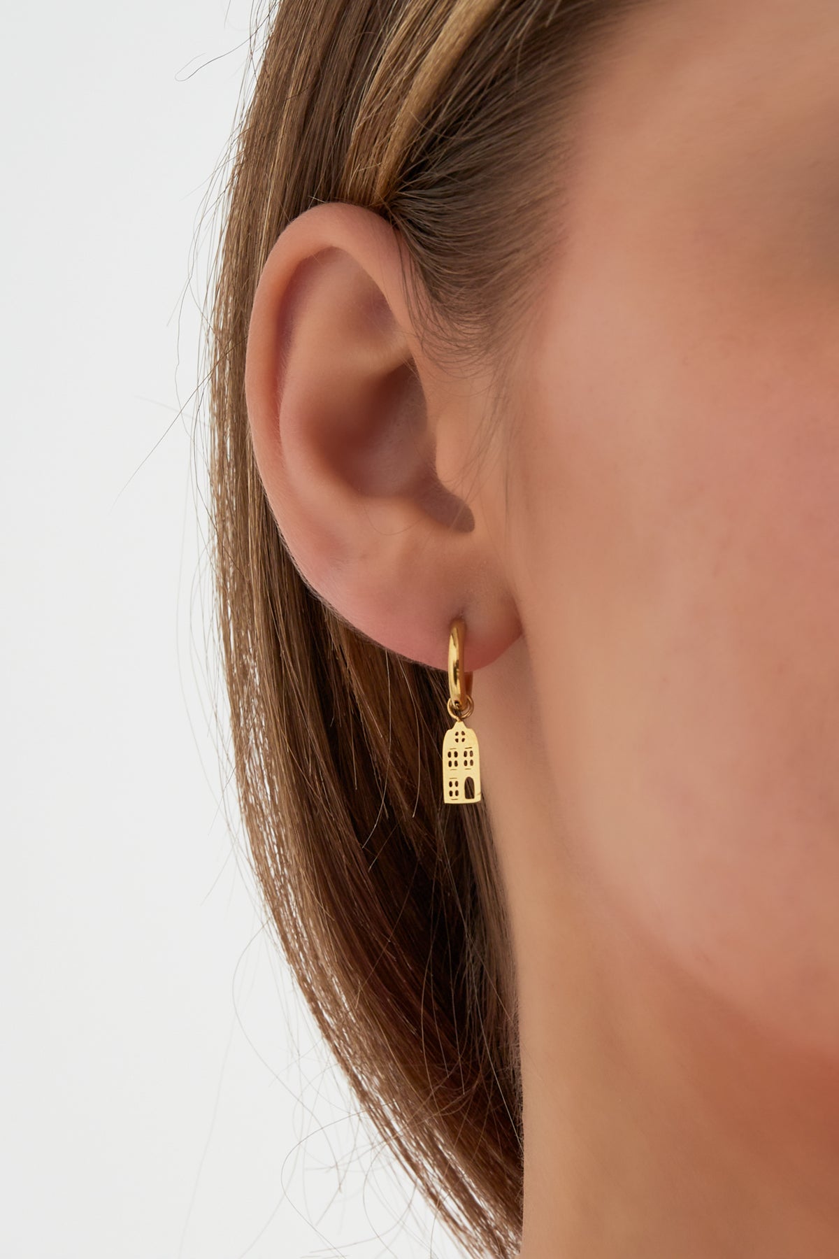 Close-up of gold drop hoop earring with architectural charm worn on a woman's ear
