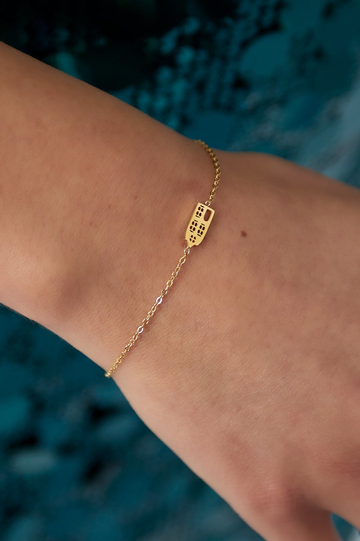Close-up view of gold domino charm bracelet worn on wrist showing fine chain and unique charm details