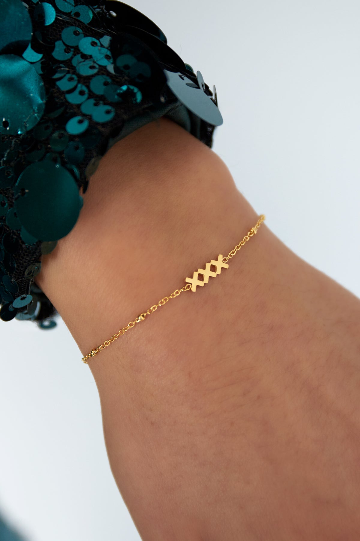 Gold charm bracelet worn on a wrist paired with a sequined sleeve, showing delicate texture