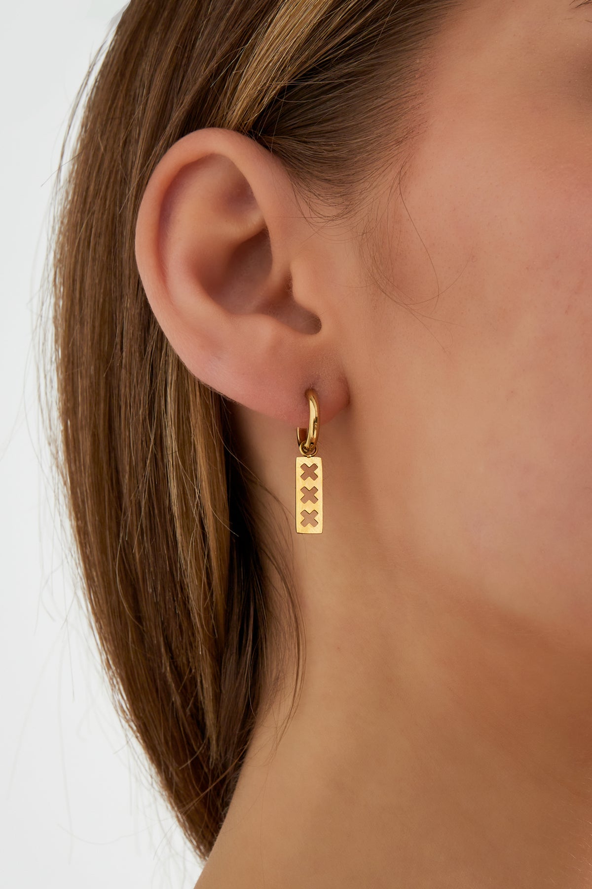 Close-up of a woman wearing one gold-toned triple cross bar drop earring