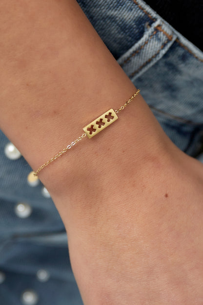 Gold triple X minimalist bracelet worn on wrist against blue denim with pearl buttons, showcasing delicate fit