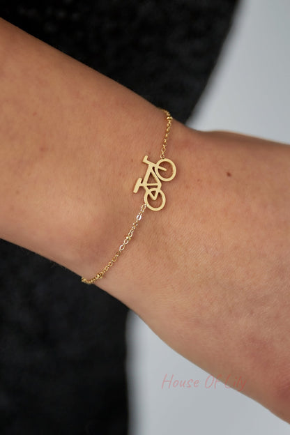 Close-up of gold bicycle charm bracelet worn on wrist, showing intricate chain and smooth bike silhouette