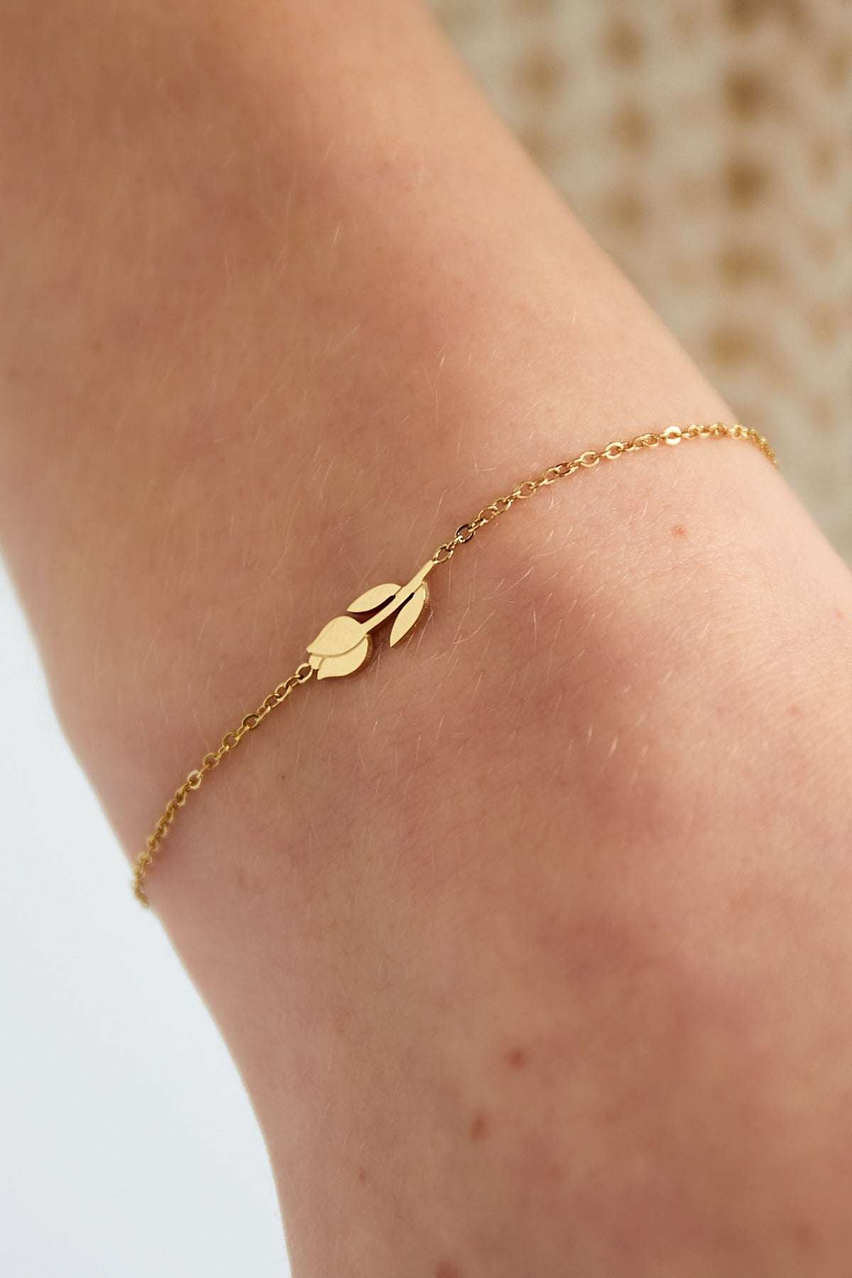 Gold tulip charm bracelet worn on a wrist, highlighting its fine chain and minimal floral design