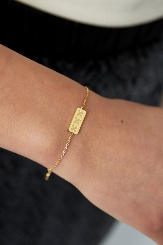 Close-up of gold triple X bracelet worn on a wrist with black and beige outfit background