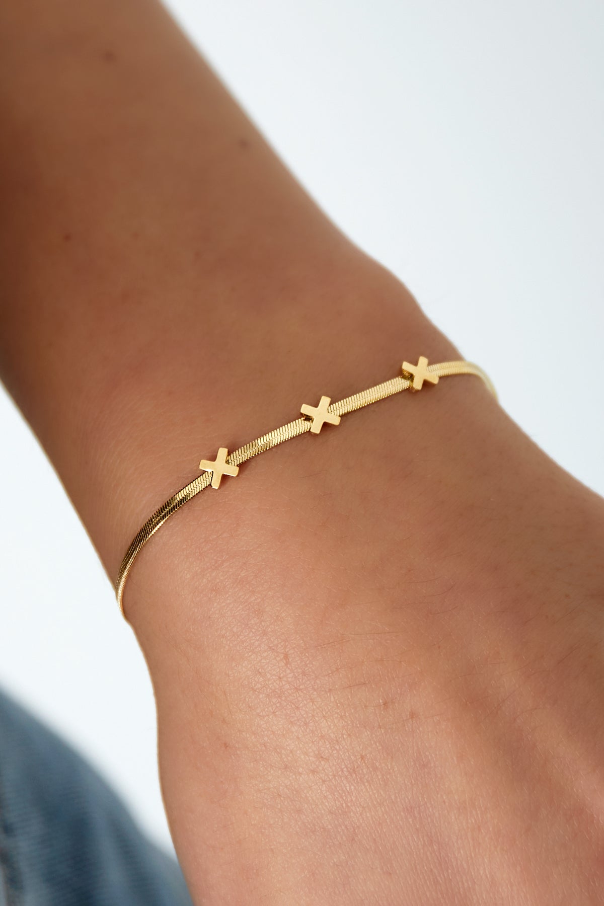 Close-up of gold triple X charm bracelet worn on wrist showcasing elegant fit