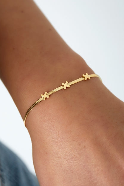 Close-up of gold triple X charm bracelet worn on wrist showcasing elegant fit