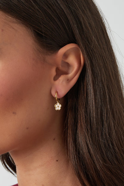 Close-up of a woman wearing a gold hoop earring with a pink enamel flower charm, showcasing a youthful and minimal style