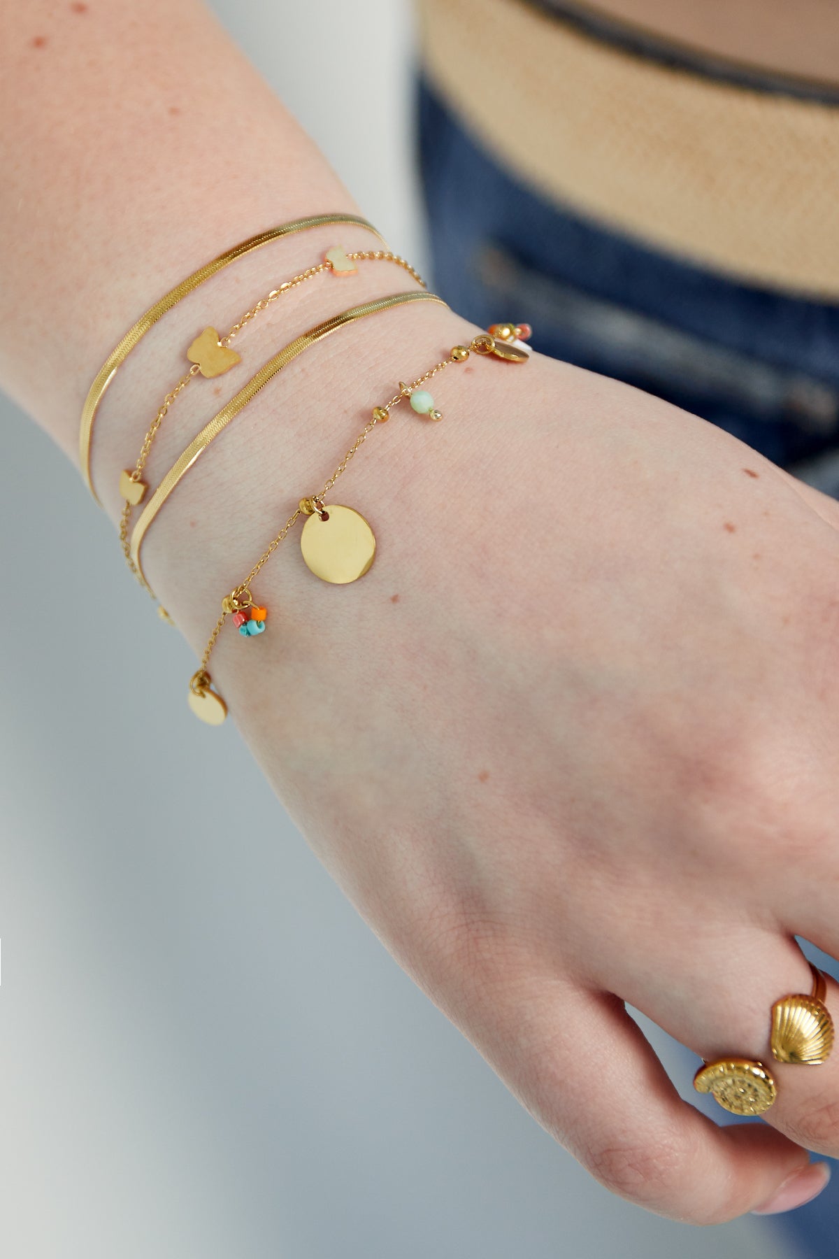 Bracelet with gold coin charms and colourful beads worn alongside matching gold bracelets and rings on a wrist