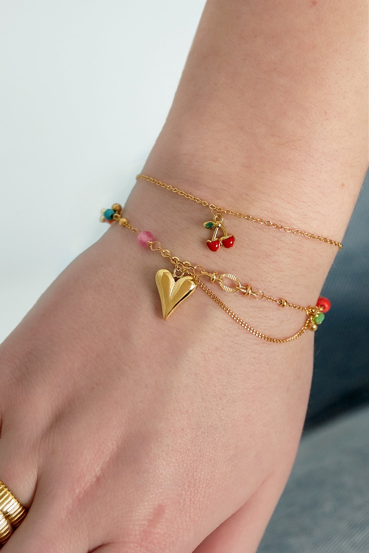 Close-up of the golden charm bracelet with heart pendant and colourful beads worn on a wrist