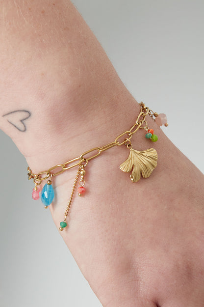 Close-up of the gold-tone vivid charm bracelet worn on wrist, featuring green leaf charm and bright beads