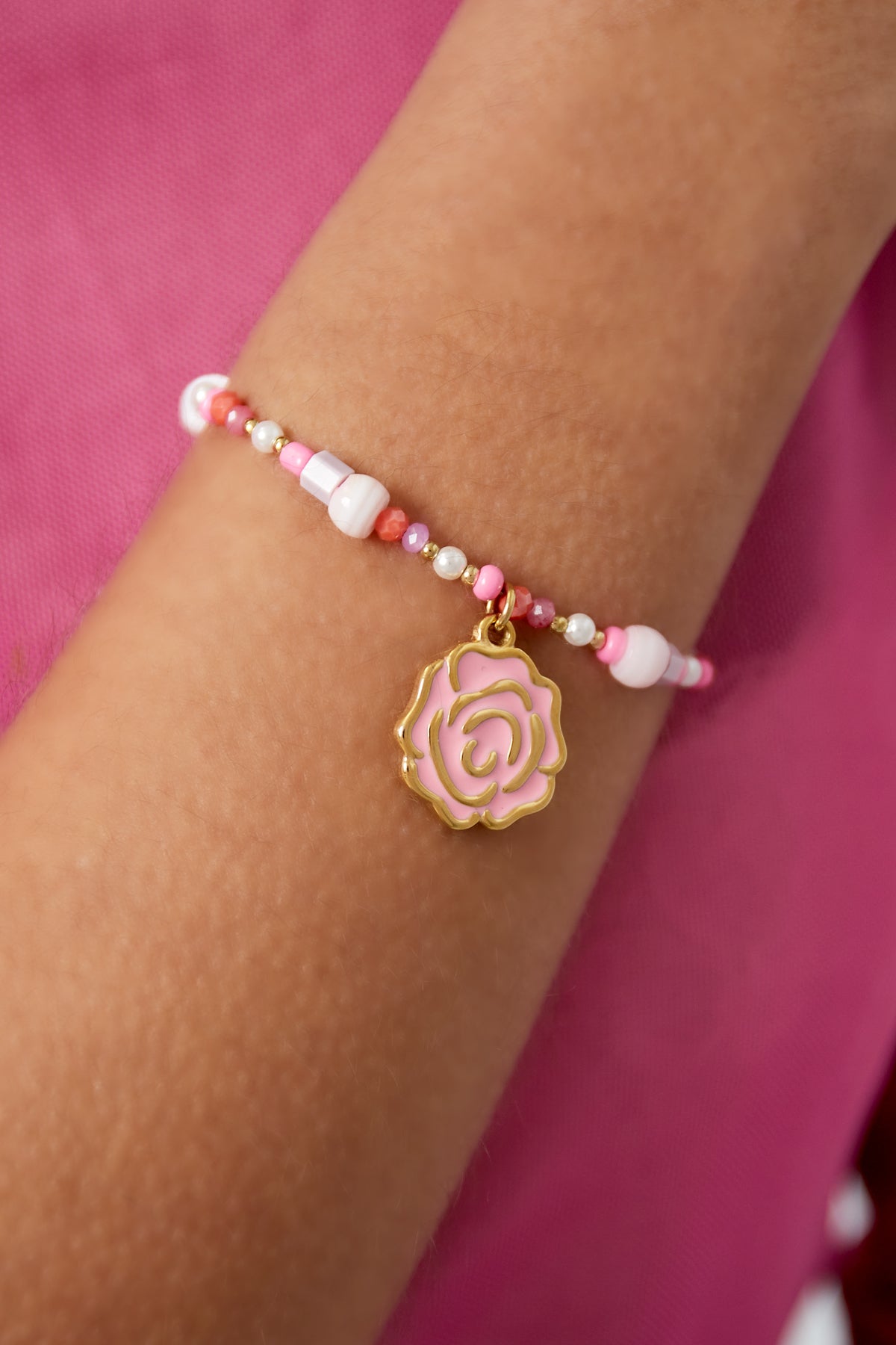 Close-up of pink rose charm beaded bracelet worn on wrist with purple fabric background