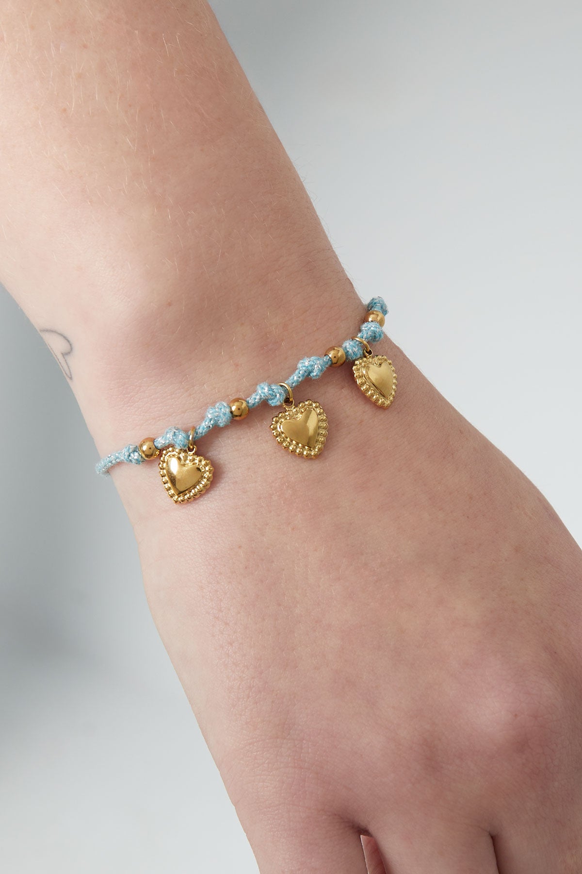 Light blue braided bracelet with gold heart charms shown on a woman's wrist