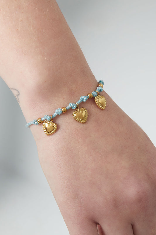 Light blue braided bracelet with gold heart charms shown on a woman's wrist