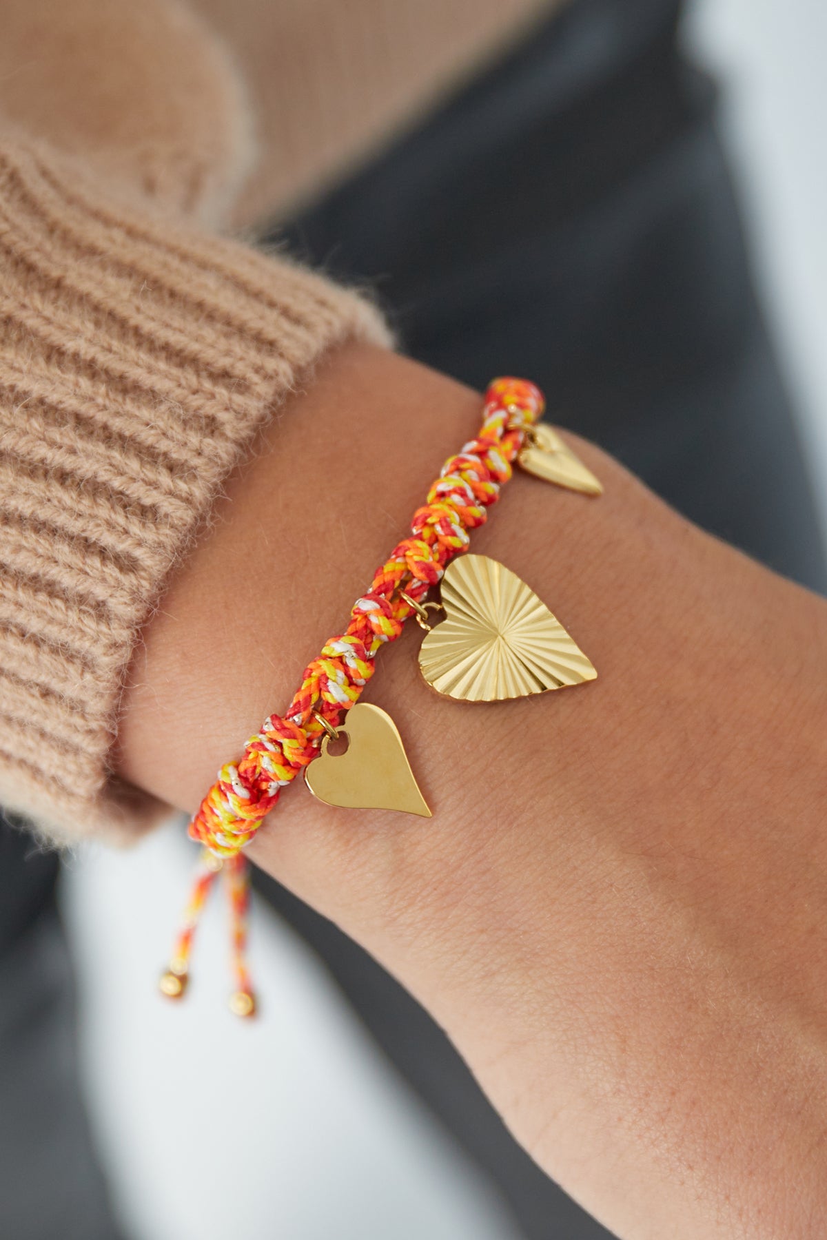 Orange braided heart charm bracelet worn on wrist paired with a beige sleeve