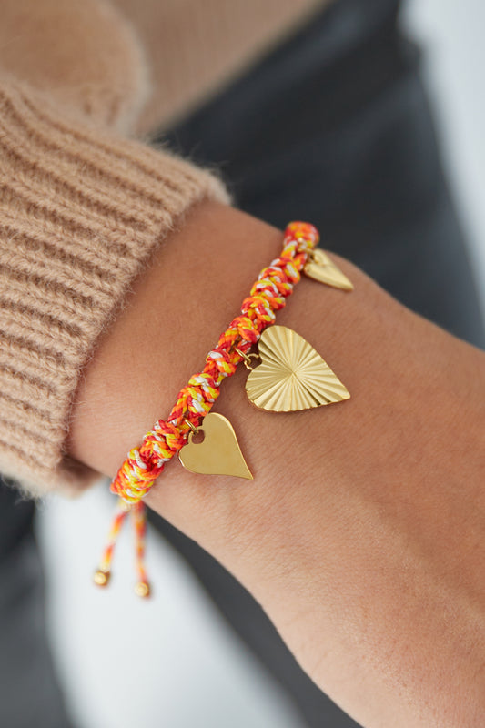 Orange braided heart charm bracelet worn on wrist paired with a beige sleeve