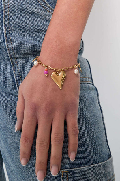 Lifestyle image showing gold-tone heart charm bracelet worn on wrist with casual denim outfit