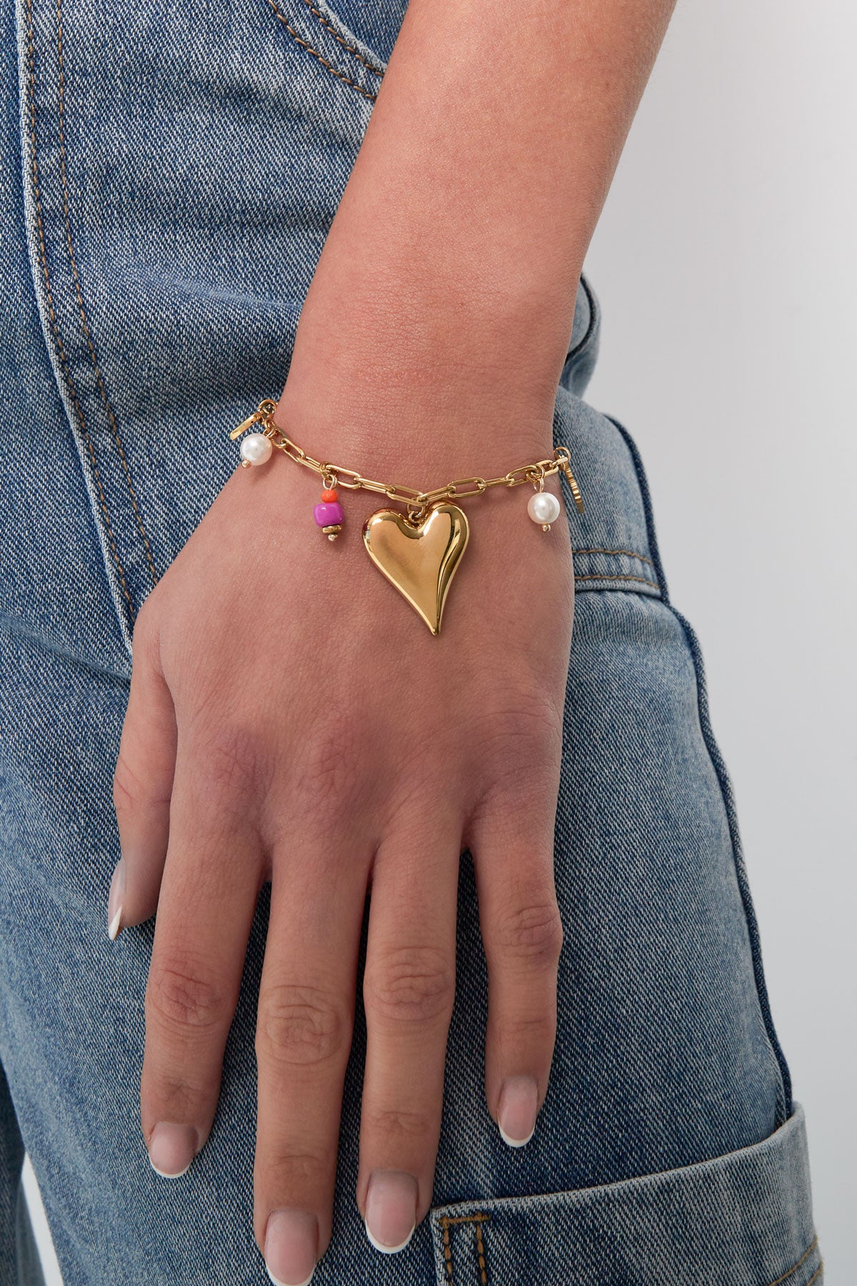 Lifestyle image showing gold-tone heart charm bracelet worn on wrist with casual denim outfit