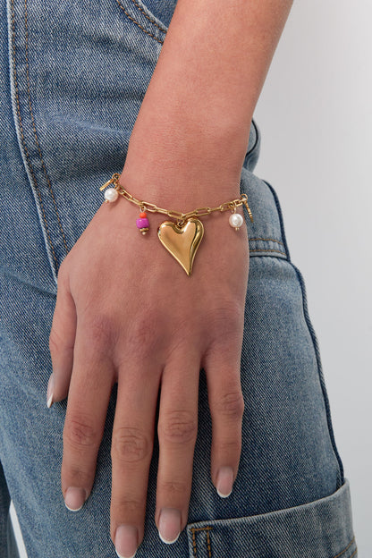 Lifestyle image showing gold-tone heart charm bracelet worn on wrist with casual denim outfit