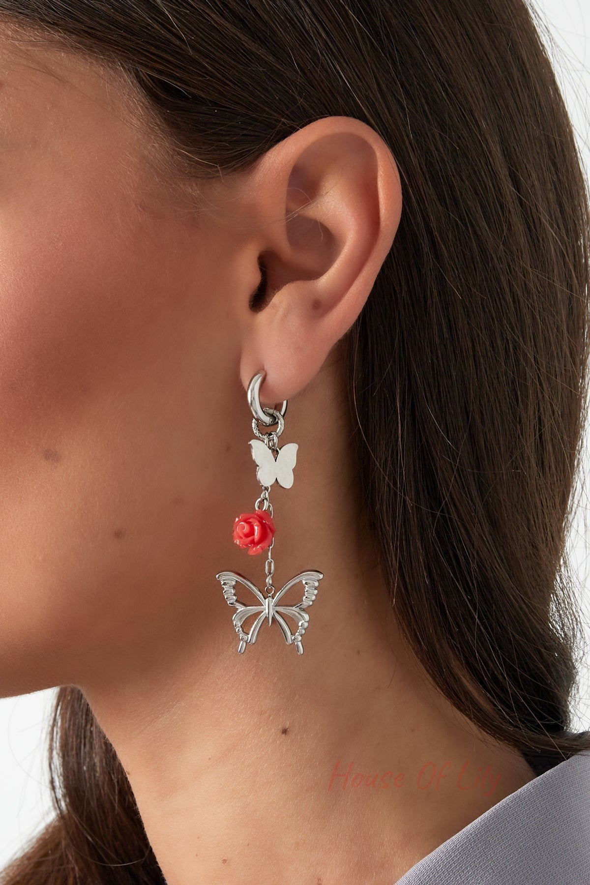 Silver butterfly and rose drop earring worn by woman with brown hair and gray top