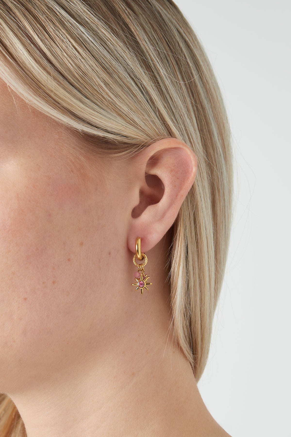 Close-up side view of gold-tone starlight charm hoop earring worn by blonde woman