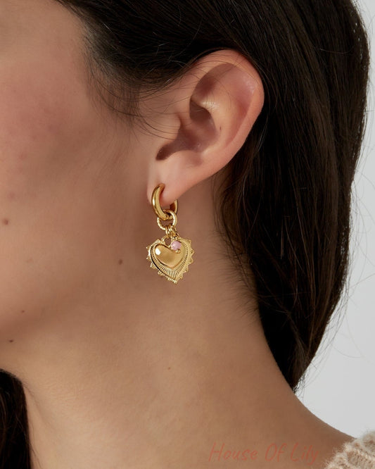 Close-up of a woman's ear wearing gold heart charm earrings with pink stone beads