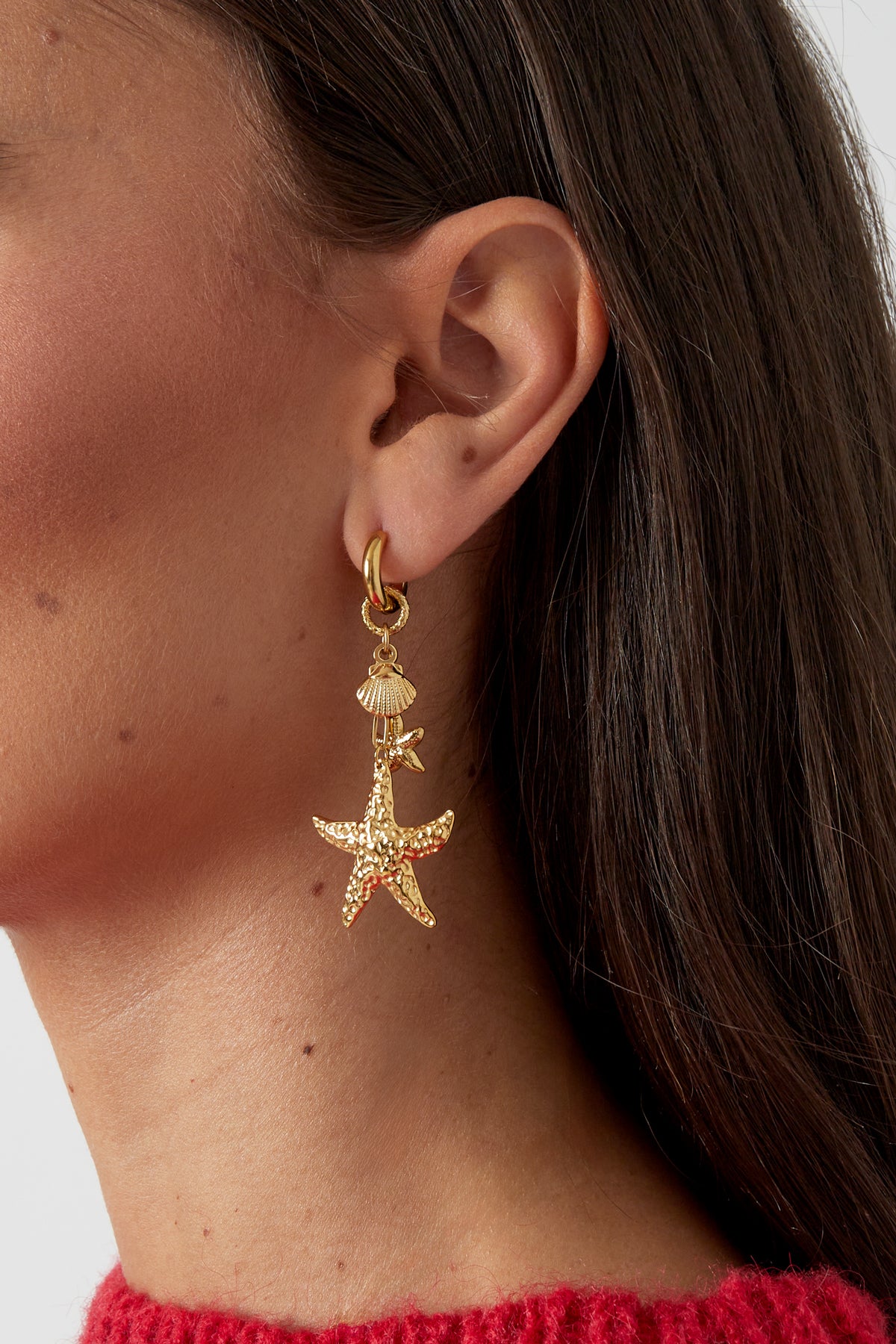 Close-up shot of gold starfish drop earring worn on a woman's ear against her dark hair and red sweater