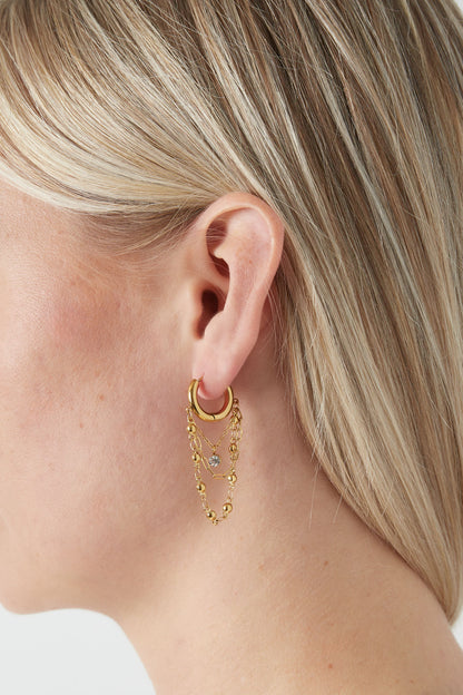 Close-up of a blonde woman wearing one gold chained hoop drop earring showing elegant layered chains