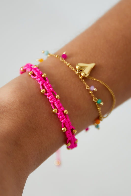 Woman's wrist wearing bright pink braided bead bracelet layered with gold and colorful charm bracelet