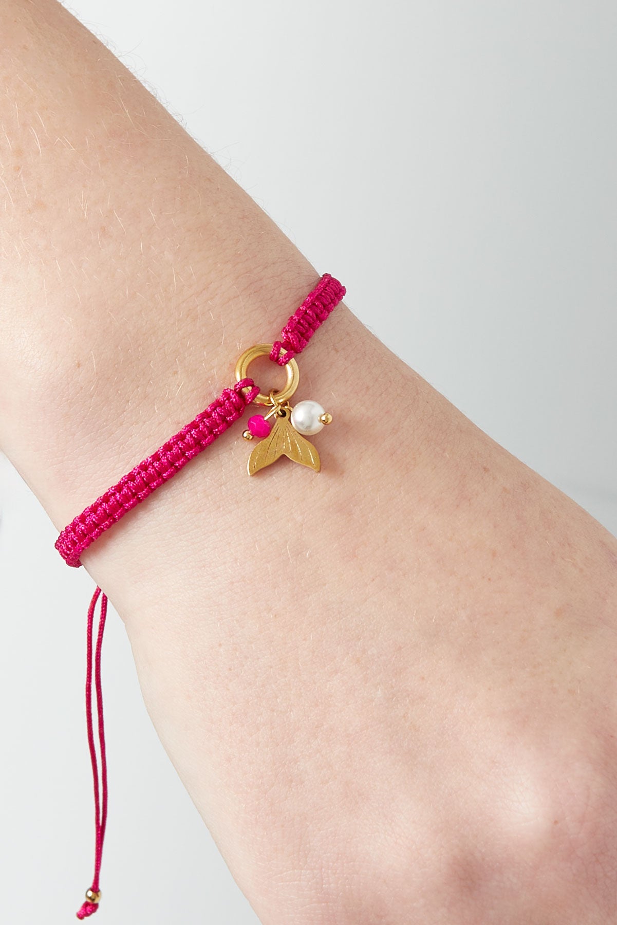 Pinkish fuchsia braided bracelet with mermaid charm worn on woman's wrist against light background