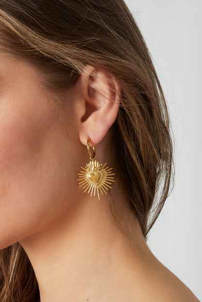 Woman wearing gold Milagros heart sunburst hoop earrings with brown hair