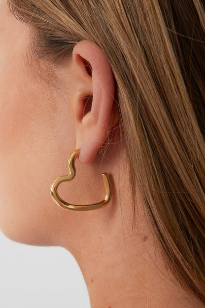 Side view of a woman wearing a gold wavy heart hoop earring