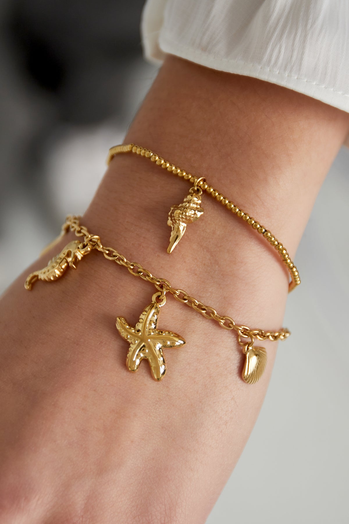Close-up of gold-tone charm bracelet and a delicate beaded bracelet worn on wrist showcasing ocean motifs
