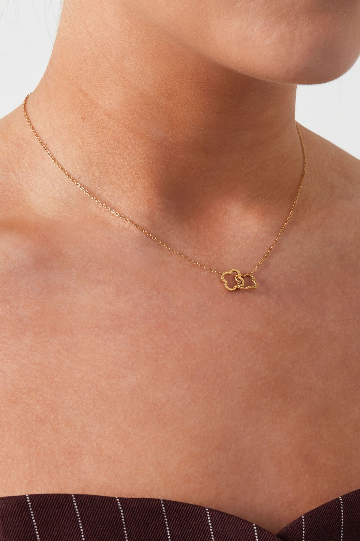 Close-up of woman wearing gold interlinked clover pendant necklace