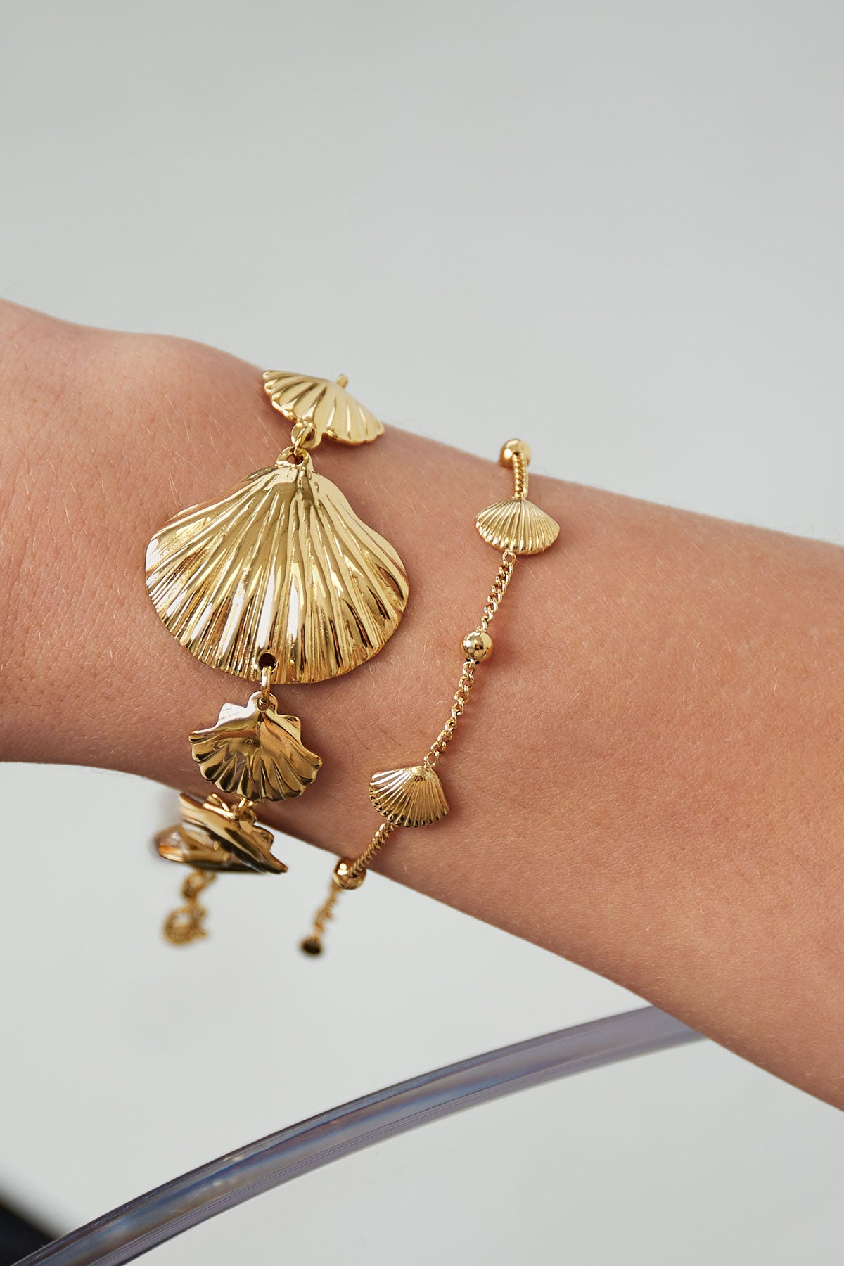 Close-up view of two gold seashell bracelets worn on wrist, showing delicate shell charms and fine chain links