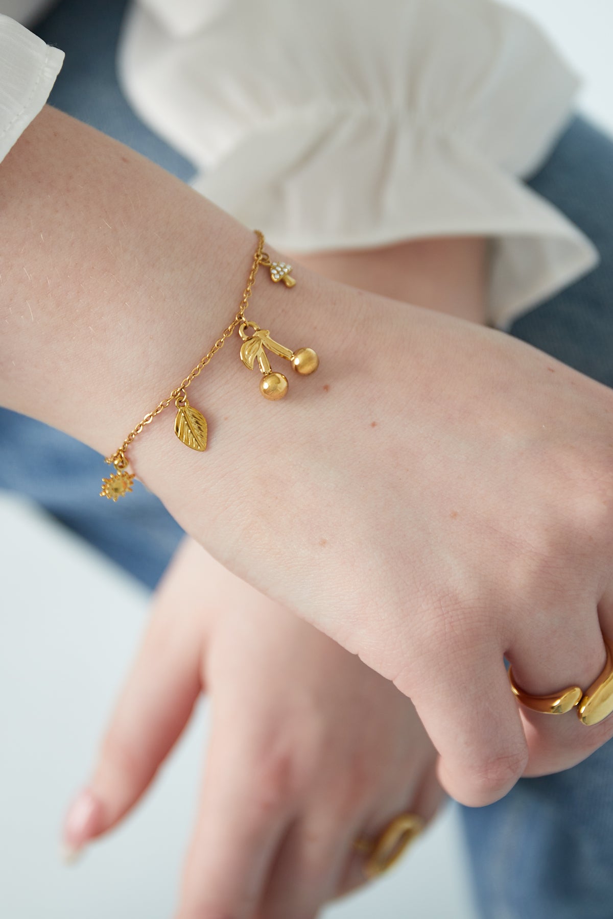 Close-up of gold charm bracelet on wrist with white shirt cuff and stylish gold rings