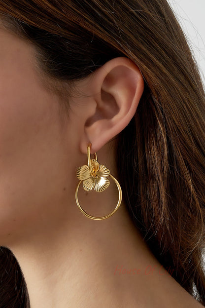 Close-up of gold-tone floral hoop drop earring worn by a woman, showing detailed flower charm and hoop
