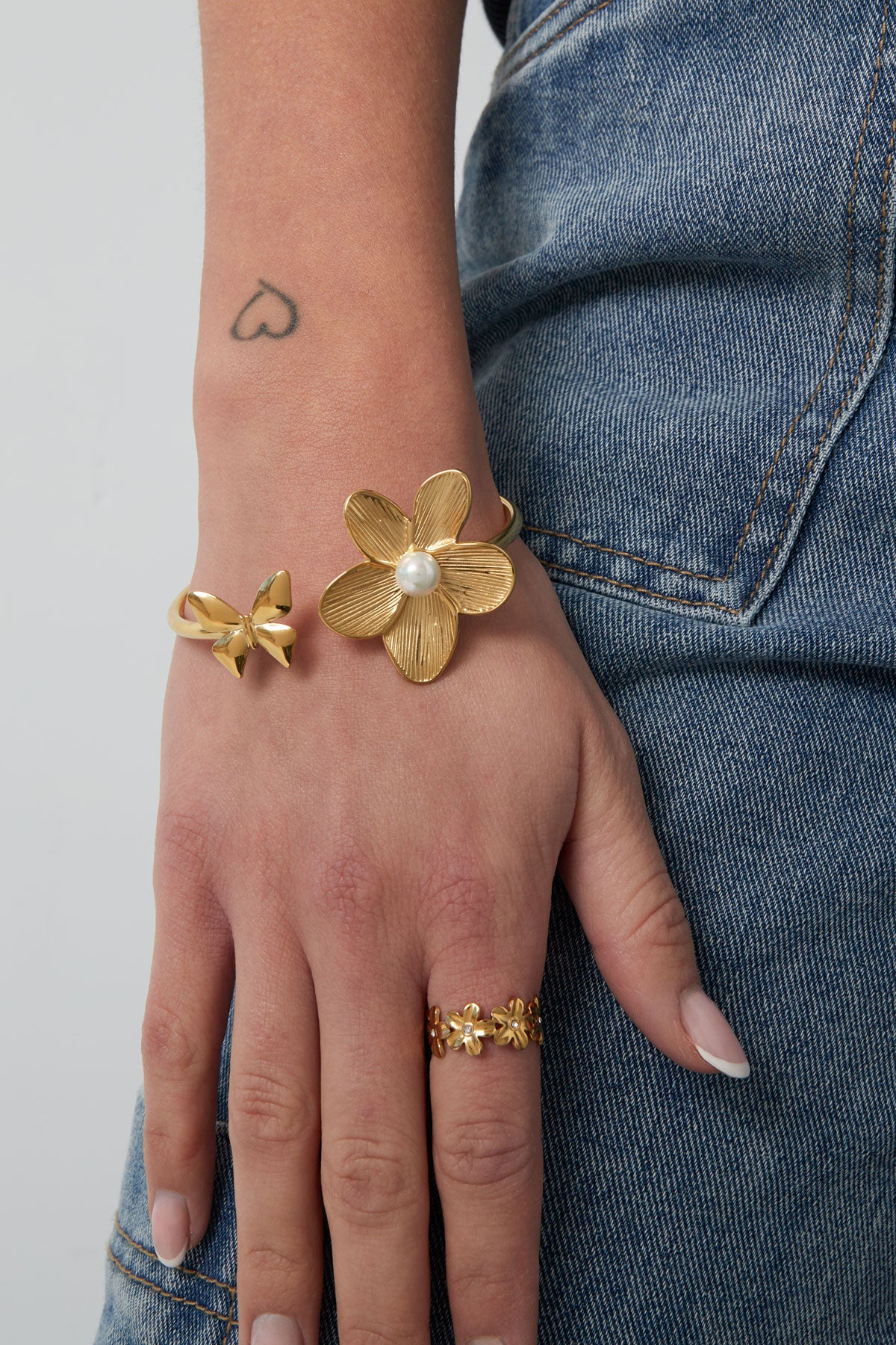 Model wearing gold butterfly flower cuff bracelet paired with gold flower ring and denim jeans