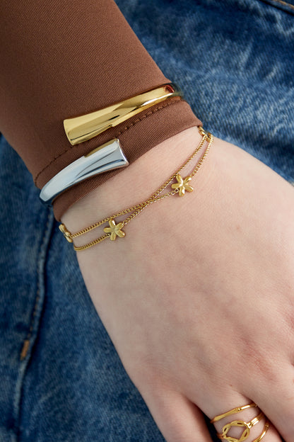 Model wearing gold and silver spiral cuff bracelets paired with layered dainty gold chain and rings