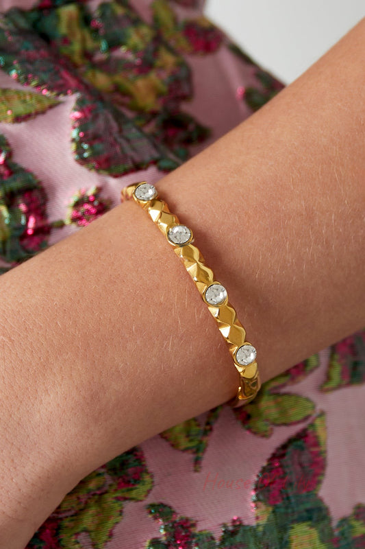 Close-up of gold tone crystal studded bangle bracelet worn on wrist with colorful floral fabric in background