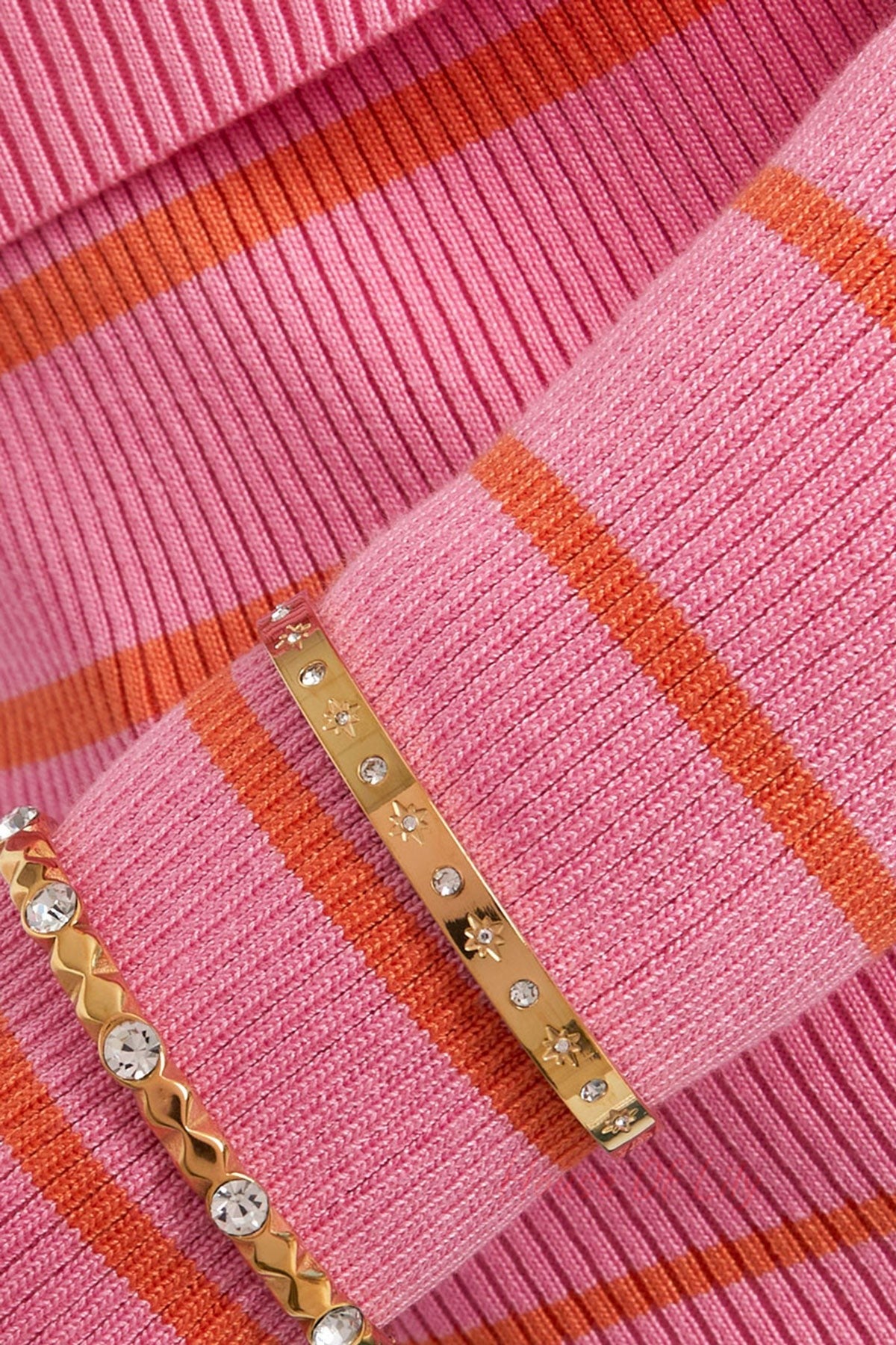Close-up of a gold-tone starry bracelet worn over a pink and orange striped sweater, paired with another crystal bracelet