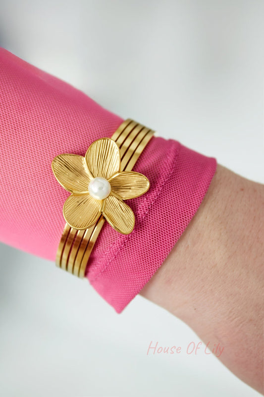 Gold-tone floral pearl bangle bracelet worn on wrist with pink sleeve, showcasing design detail and fit