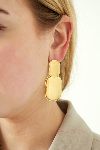 Close-up of a woman wearing shiny gold modern double drop earrings highlighting their polished surface and size