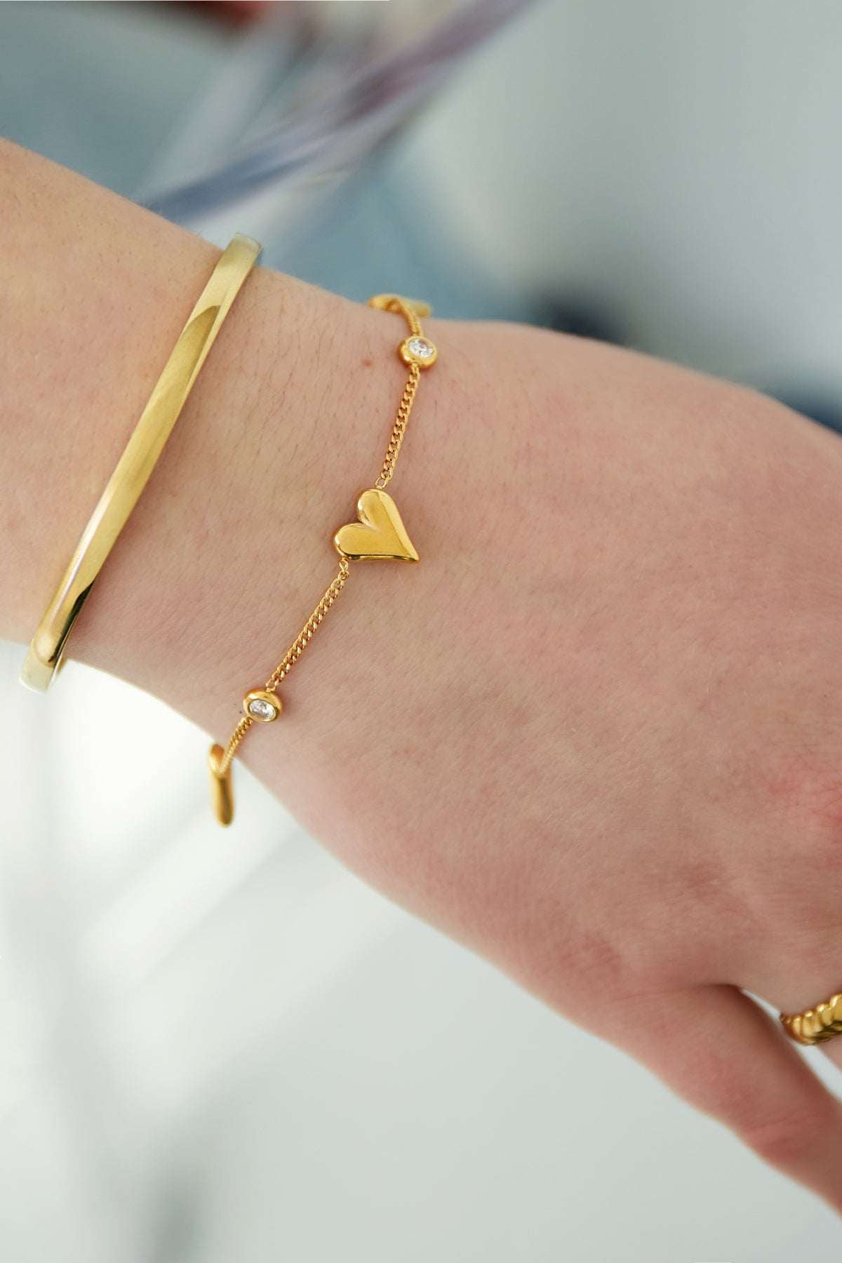 Close-up of gold heart bracelet worn on wrist alongside a gold bangle