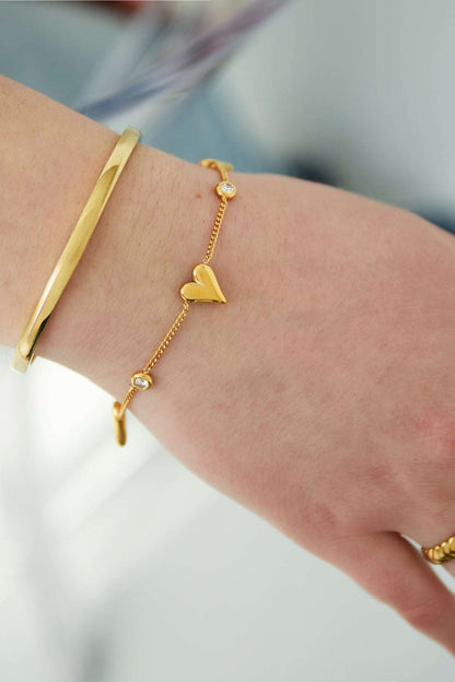 Close-up of gold heart bracelet worn on wrist alongside a gold bangle