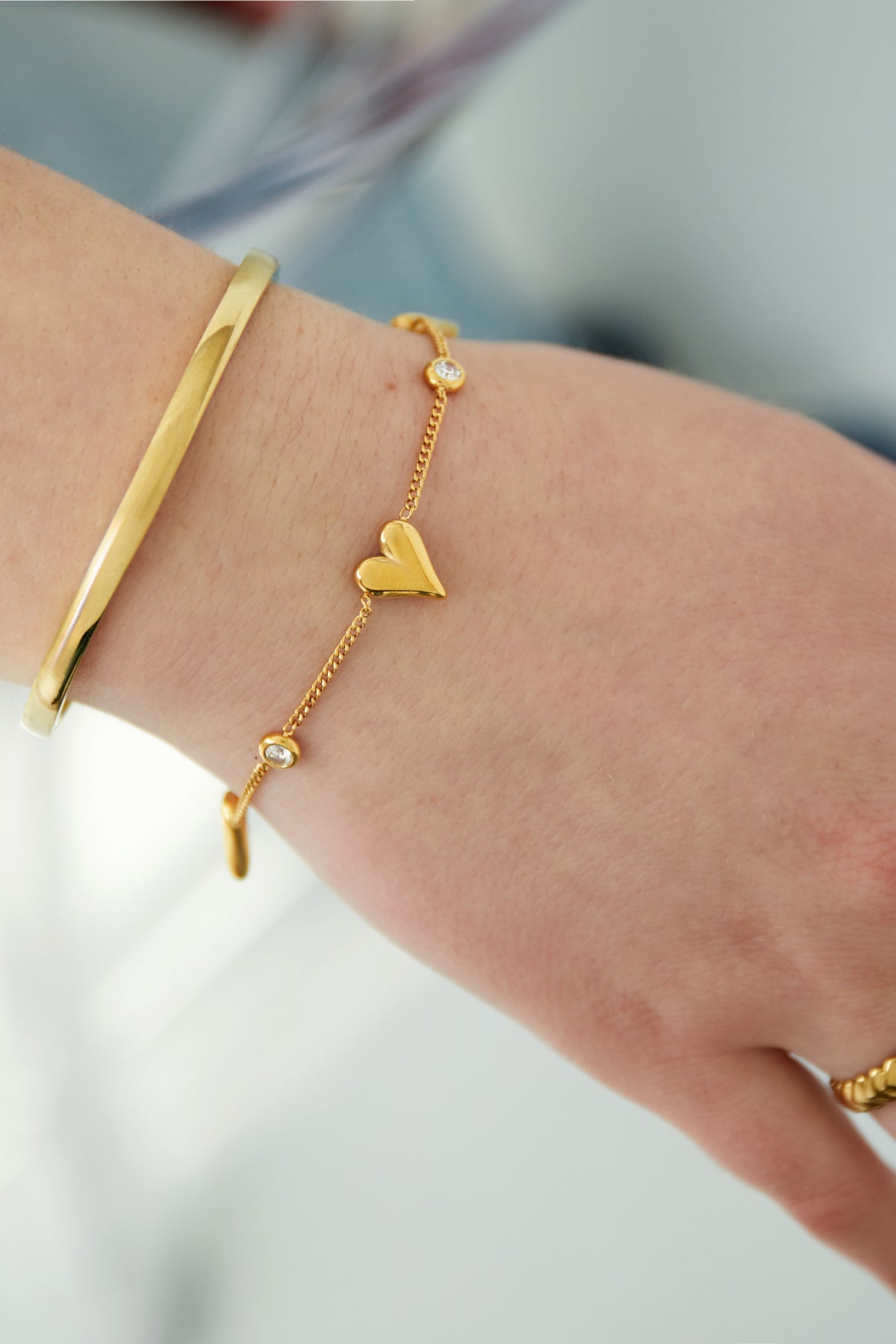 Close-up of gold heart bracelet worn on wrist alongside a gold bangle