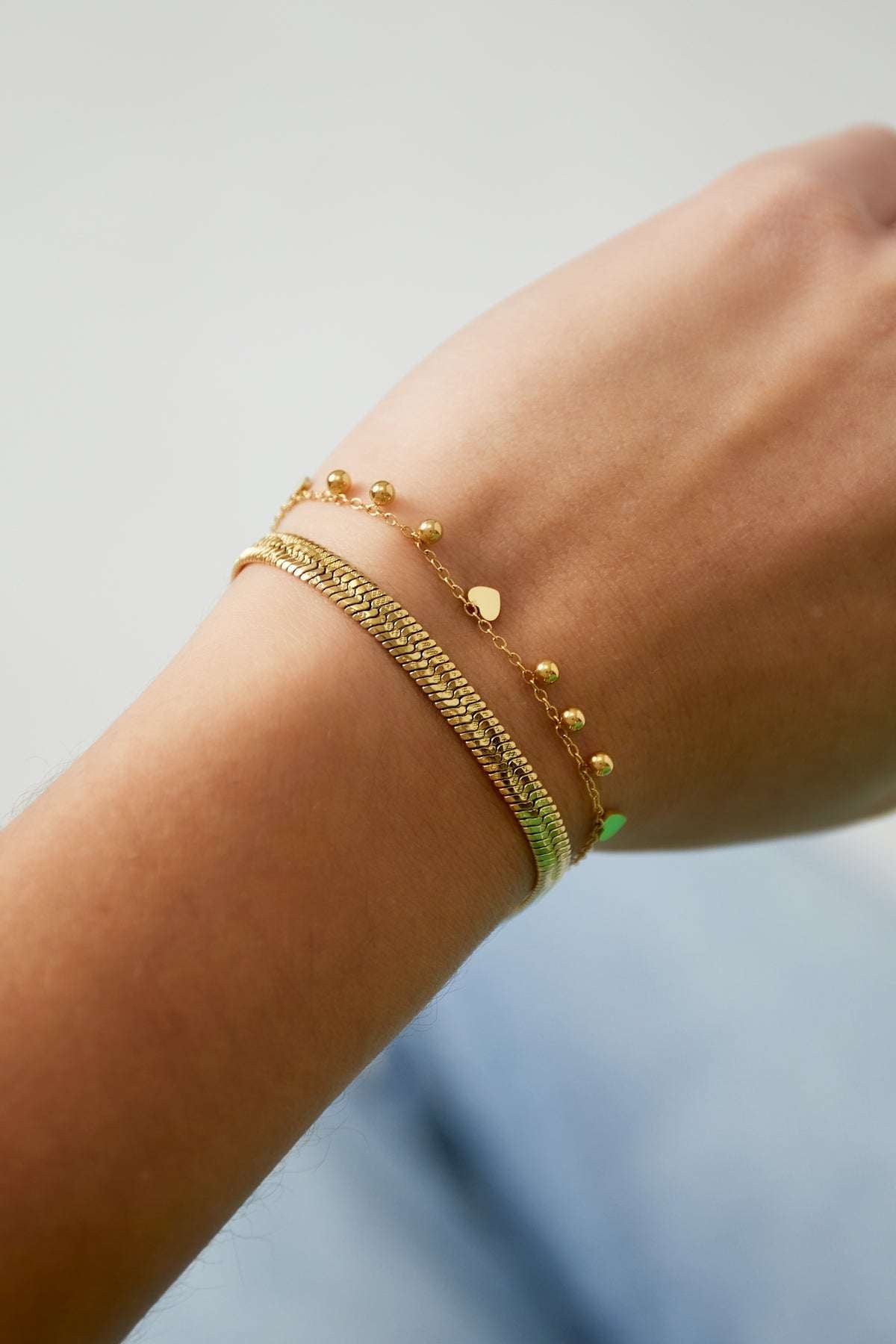 Close-up of a wrist wearing the delicate gold heart charm bracelet alongside a textured gold bangle