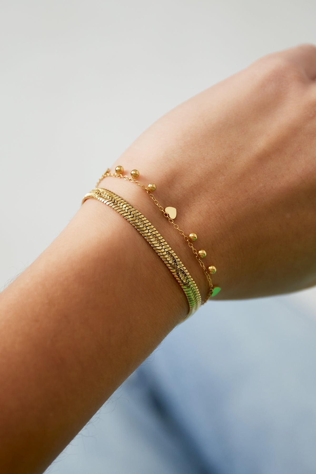 Close-up of a wrist wearing the delicate gold heart charm bracelet alongside a textured gold bangle